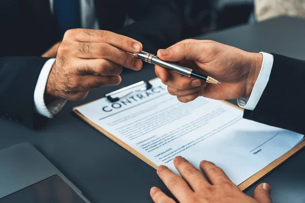 stock image Two businesspeople sit across the desk as business deal is taking place. Corporate attorney giving a pen for client or partner to sign contract paper, sealing the deal with signature. Fervent