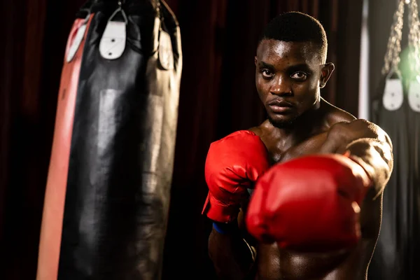stock image Boxing fighter shirtless posing, African American Black boxer punch his fist in aggressive stance and ready to fight at gym with kicking bag and boxing equipment in background. Impetus