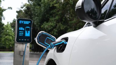 Elektrikli araba, çevre yeşil parkındaki elektrik kablosu ve yeşillik yeşili yeşillik yapraklarıyla şarj etmek için şarj istasyonuna bağlandı. Geleceğin yenilikçi her arabası ve enerji sürdürülebilirliği.