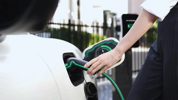 ビジネスマンは 市内中心部や公共駐車場の充電ステーションから彼女の電気自動車を充電します 代替クリーンエネルギーを使用して環境に優しい充電式車 Peruse — ストック写真