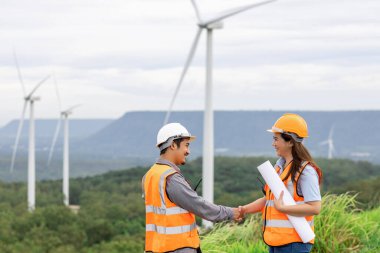 Erkek ve kadın mühendisler kırsal kesimdeki bir tepenin tepesinde ya da dağda rüzgar çiftliğinde çalışıyorlar. Yenilenebilir ve sürdürülebilir enerjinin gelecekteki üretimi için yenilikçi idealler.