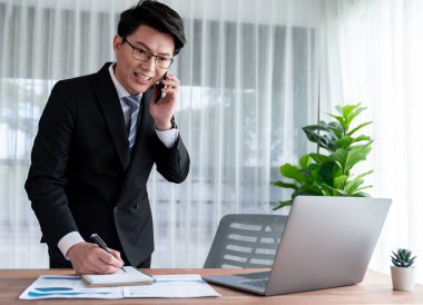 Ofis masasında akıllı telefonuyla bilgisayar başında çalışan bir iş adamı. Akıllı bir yönetici finansal iş verilerini araştırıyor ya da stratejik işler planlıyor, telefonla konuşuyor. Sevinçli.