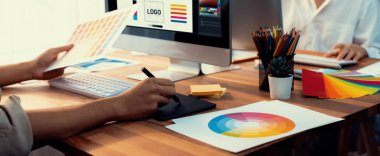 Grafik tasarımcısı, modern dijital stüdyo işyerinde profesyonel grafik ekibiyle benzersiz bir tasarım yaparken bilgisayar dizüstü bilgisayar ve grafik çizim kalemi üzerinde çalışır. Panorama çekimi. İnceleyin