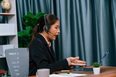 Bilgisayarında mikrofon ve kulaklıkla Asyalı çağrı merkezi çalışıyor. Kadın operatör istisnai müşteri hizmetleri sunar. Destek veren çağrı merkezi ajanı, müşteriye soruşturmada yardım ediyor. Coşkulu.
