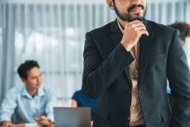 İş adamı, toplantı odasının arka planında çeşitli iş arkadaşlarıyla güven içinde poz veriyor. Çok kültürlü ekip iş başarısı için birlikte çalışır. Modern iş adamı portresi. Uyum