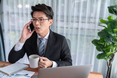 Ofis masasında akıllı telefonuyla bilgisayar başında çalışan bir iş adamı. Akıllı bir yönetici finansal iş verilerini araştırıyor ya da stratejik işler planlıyor, telefonla konuşuyor. Sevinçli.
