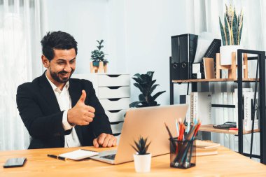 Siyah takım elbise giymiş heyecanlı ve mutlu bir iş adamı başarılı bir iş tanıtımı, enerji ve neşe kazandıktan sonra ofis masasında kutlama jesti olarak elini kaldırır. Coşkulu