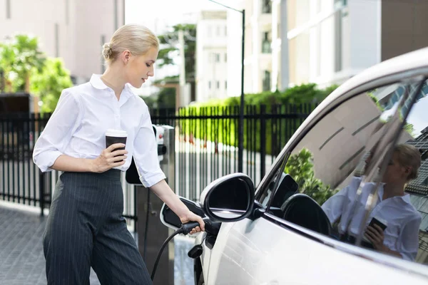 Businesswoman Drinking Coffee Leaning Electric Vehicle Recharging Public Charging Station — Foto Stock
