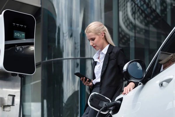 Businesswoman Wearing Black Suit Using Smartphone Leaning Electric Car Recharge — Stock Fotó