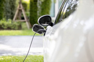Closeup electric vehicle plugged-in with cable from charging point powered for progressive concept by alternative clean energy rechargeable EV car at home charging station.