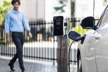 Progressive eco-friendly concept of focus parking EV car at public electric-powered charging station in city center with blur businessman walking in the background.