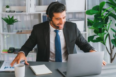 Erkek çağrı merkezi operatörü ya da telesales temsilcisi ofis masasında otururken kulaklık takıyor ve müşteri desteği sağlayan ya da ikna edici satış yapan müşteriyle sohbet ediyor. coşkulu