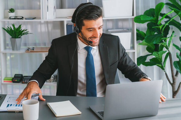 Мужчина оператор колл-центра или представитель телесалов, сидящий на своем рабочем столе в наушниках и в разговоре с клиентом, обеспечивая поддержку обслуживания клиентов или делая убедительные продажи. пылкий