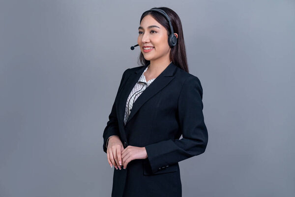 Asian female call center operator with happy smile face advertises job opportunity on empty space, wearing formal suit and headset on customizable isolated background for job recruitment. Jubilant