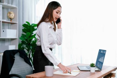 Genç hevesli iş kadını iş görüşmesinde konuşuyor ve laptopuna çoklu ofis hanımı olarak notlar yazıyor. Müşterilerle telefonda konuşurken iş ödevleri yazan kadın çalışan.
