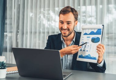 Siyah takım elbiseli profesyonel işadamı, online sunum toplantısında finansal verileri veya BI kağıt panosunu laptop kamerasına sunar. Ofiste sanal toplantı sunumuyla uzaktan çalışma. Varlık