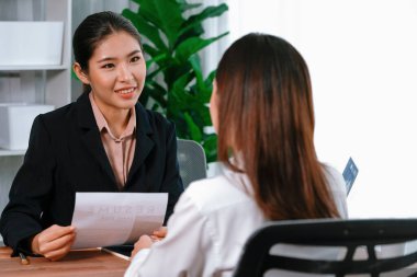 İki Asyalı kadın ofiste iş görüşmesi yapıyor. Başvuranlar özgeçmişi ve iş başvurusu hakkında konuşurken resmi takım giyerler. Muhabir olumlu ve konuşkan bir şekilde sorgulama talep ediyor. Coşkulu.