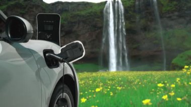 Elektrikli araba, doğal ortam, şelale ve akış arkaplanındaki şarj istasyonundan enerji yüklüyor. Yenilenebilir enerji kaynaklı EV otomobillerin enerji sürdürülebilirliği kavramı.