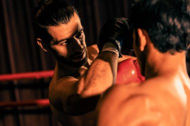 Asyalı ve Kafkasyalı Muay Thai boksörü boks maçında dirsek atağı yapıyor. Güçlü kaslı bir boksör acımasız bir dövüş hüneriyle yumruk ve dirsek yumruğa dövüşüyor. Impetus