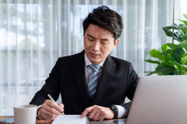 Ofis masasında dizüstü bilgisayarda çalışan bir iş adamı. Akıllı yönetici finansal iş verilerini araştırıyor ya da masada bilgisayarla stratejik iş pazarlaması planlıyor. Sevinçli.