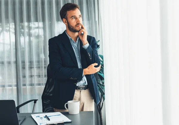 黒のスーツを着たハンサムなビジネスマンは 彼の次の動きについて戦略的に考えて 彼の現代的なオフィスの肖像画で自信を持って立っている エンティティ — ストック写真