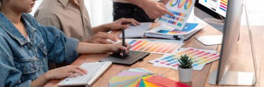 Grafik tasarımcısı, modern dijital stüdyo işyerinde profesyonel grafik ekibiyle benzersiz bir tasarım yaparken bilgisayar dizüstü bilgisayar ve grafik çizim kalemi üzerinde çalışır. Panorama çekimi. İnceleyin