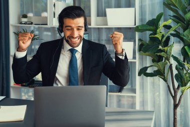 Siyah takım elbiseli heyecanlı ve mutlu iş adamı, ofis masasında kutlama jesti olarak kolunu kaldırdı. İş yerinde başarılı bir çağrı merkezi ya da telesales operatörü kutlama yapıyor. Coşkulu