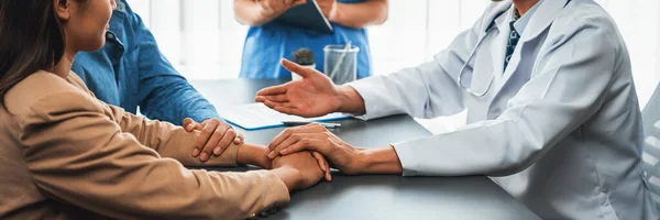 Arzt Der Mitfühlende Gesundheitsberatung Anbietet Während Junge Paarpatienten Händchen Halten — Stockfoto