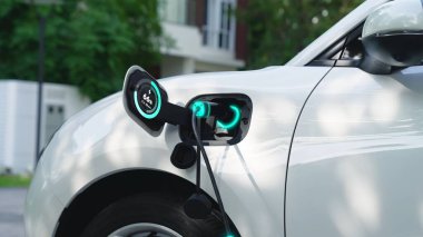 EV charger from home charging station plugged in and recharging electric car displaying digital battery status hologram. Smart and futuristic home energy infrastructure. Peruse clipart