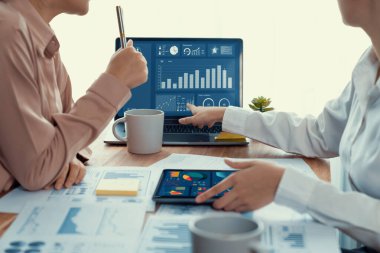 Analist ekip arkadaşı dijital gösterge panelinde finansal verileri tartışır, grafikleri dizüstü bilgisayar ve tablet ekranda analiz eder. Modern ofis pazarlama planlamak için iş zekasını kullanır. Coşkulu.