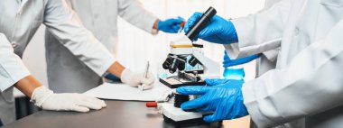 Kendini adamış bir grup bilim adamı yeni bir aşı ilacı ya da antibiyotik geliştirmek için tıbbi laboratuvarda mikroskop kullanarak kimyasal deney yapıyorlar. Biyoteknoloji laboratuvarı ve tıp araştırma konsepti. Neoterik