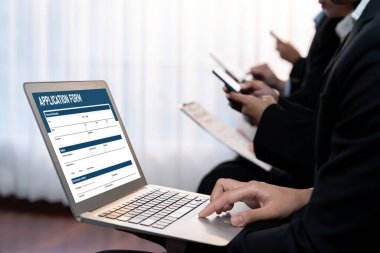 İş başvurusu yapan kişi diğer adaylarla iş görüşmesi için bekleme odasında otururken şirket şirketinde dizüstü bilgisayarla iş başvurusunda bulunuyor. Modern iş arayanlar ve iş arayanlar. Önde.