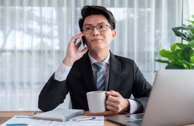 Ofis masasında akıllı telefonuyla bilgisayar başında çalışan bir iş adamı. Akıllı bir yönetici finansal iş verilerini araştırıyor ya da stratejik işler planlıyor, telefonla konuşuyor. Sevinçli.