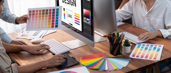 Graphic designer work on computer laptop and with graphic drawing pen while brainstorming unique design with professional graphic team in modern digital studio workplace. Panorama shot. Scrutinize