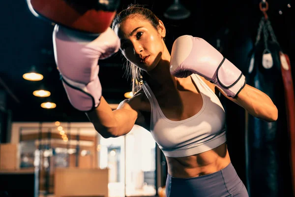 stock image Asian female Muay Thai boxer punching in fierce boxing training session, delivering strike to her sparring trainer wearing punching mitts, showcasing Muay Thai boxing technique and skill. Impetus