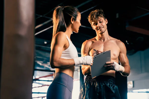 Stock image Asian female Muay Thai boxer and her personal boxing trainer discussing on her physical progress in the gym reflecting commitment to her body muscle growth and boxing performance. Impetus