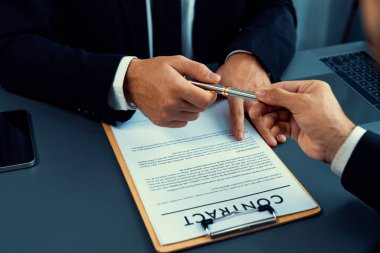 İş anlaşması yapılırken iki işadamı masanın karşısında oturuyor. Şirket avukatı, sözleşmeyi imzalaması için müvekkiline ya da ortağına kalem veriyor ve anlaşmayı imzayla imzalıyor. Coşkulu