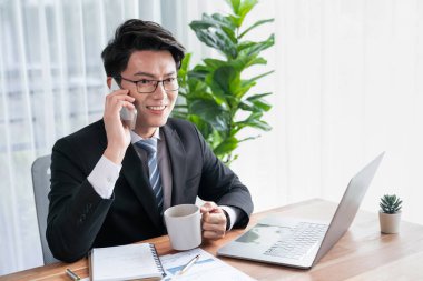Ofis masasında akıllı telefonuyla bilgisayar başında çalışan bir iş adamı. Akıllı bir yönetici finansal iş verilerini araştırıyor ya da stratejik işler planlıyor, telefonla konuşuyor. Sevinçli.