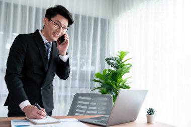 Ofis masasında akıllı telefonuyla bilgisayar başında çalışan bir iş adamı. Akıllı bir yönetici finansal iş verilerini araştırıyor ya da stratejik işler planlıyor, telefonla konuşuyor. Sevinçli.