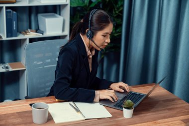 Bilgisayarında mikrofon ve kulaklıkla Asyalı çağrı merkezi çalışıyor. Kadın operatör istisnai müşteri hizmetleri sunar. Destek veren çağrı merkezi ajanı, müşteriye soruşturmada yardım ediyor. Coşkulu.