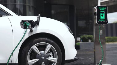 Şehir merkezinin otoparkındaki şarj istasyonuna bağlı elektrikli araba. Alternatif temiz ve sürdürülebilir enerji kullanan geleceğin yenilikçi yenilenebilir EV arabası. İnceleyin