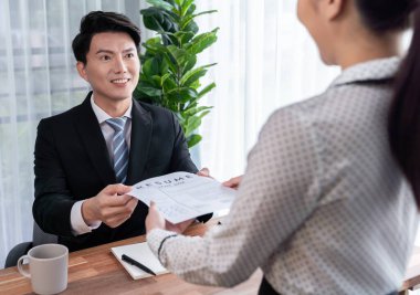 Asyalı kadın adayın iş görüşmesi sırasında iş başvurusu için gerekli nitelikleri sunması için özgeçmişini ya da özgeçmişini İK müdürüne vermesi. Sevinçli.