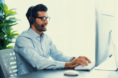 Erkek çağrı merkezi operatörü ya da telesales temsilcisi ofis masasında oturmuş kulaklık takıyor ve müşteri hizmetleri desteği sağlayan ya da satış yapan müşteriyle sohbet ediyor. coşkulu