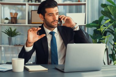 Çalışkan işadamı, ofisindeki dizüstü bilgisayarla cep telefonlu, modern, çalışkan ofis çalışanı yaşam biçimi konsepti olarak çalışırken müşterileriyle telefonda konuşmakla meşgul. Coşkulu