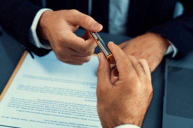 İş anlaşması yapılırken iki işadamı masanın karşısında oturuyor. Şirket avukatı, sözleşmeyi imzalaması için müvekkiline ya da ortağına kalem veriyor ve anlaşmayı imzayla imzalıyor. Coşkulu