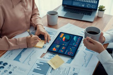 Analist ekip arkadaşı dijital gösterge panelinde finansal verileri tartışır, grafikleri dizüstü bilgisayar ve tablet ekranda analiz eder. Modern ofis pazarlama planlamak için iş zekasını kullanır. Coşkulu.