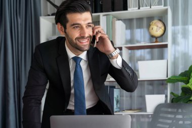 Çalışkan işadamı, ofisindeki dizüstü bilgisayarla cep telefonlu, modern, çalışkan ofis çalışanı yaşam biçimi konsepti olarak çalışırken müşterileriyle telefonda konuşmakla meşgul. Coşkulu