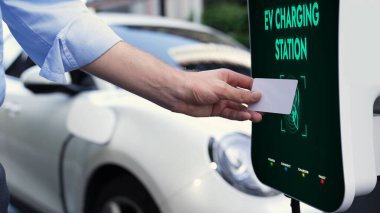İşadamı elektrikli araçlara eko-dost ve sürdürülebilir enerji tarama kredi kartı ödemesi yapıyor. Şarj edilebilir elektrikli aracına şarj noktasında güç vermek için yapılan ödeme. İnceleyin
