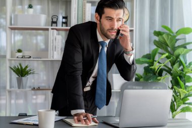 Çalışkan işadamı, ofisindeki dizüstü bilgisayarla cep telefonlu, modern, çalışkan ofis çalışanı yaşam biçimi konsepti olarak çalışırken müşterileriyle telefonda konuşmakla meşgul. Coşkulu