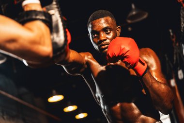 Afrika kökenli siyah boksör antrenöre yumruk atıyor ya da spor salonunda boks çantası olarak boks eldiveni takıyor. Profesyonel boks maçı için güç ve dayanıklılık eğitimi. Impetus